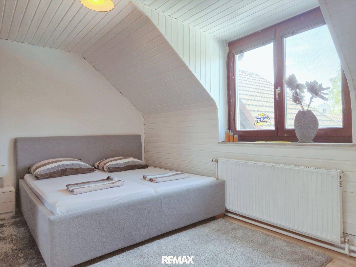 Gemütliches Schlafzimmer im Dachgeschoss mit Holzboden, Dachschrägen und Fenster.