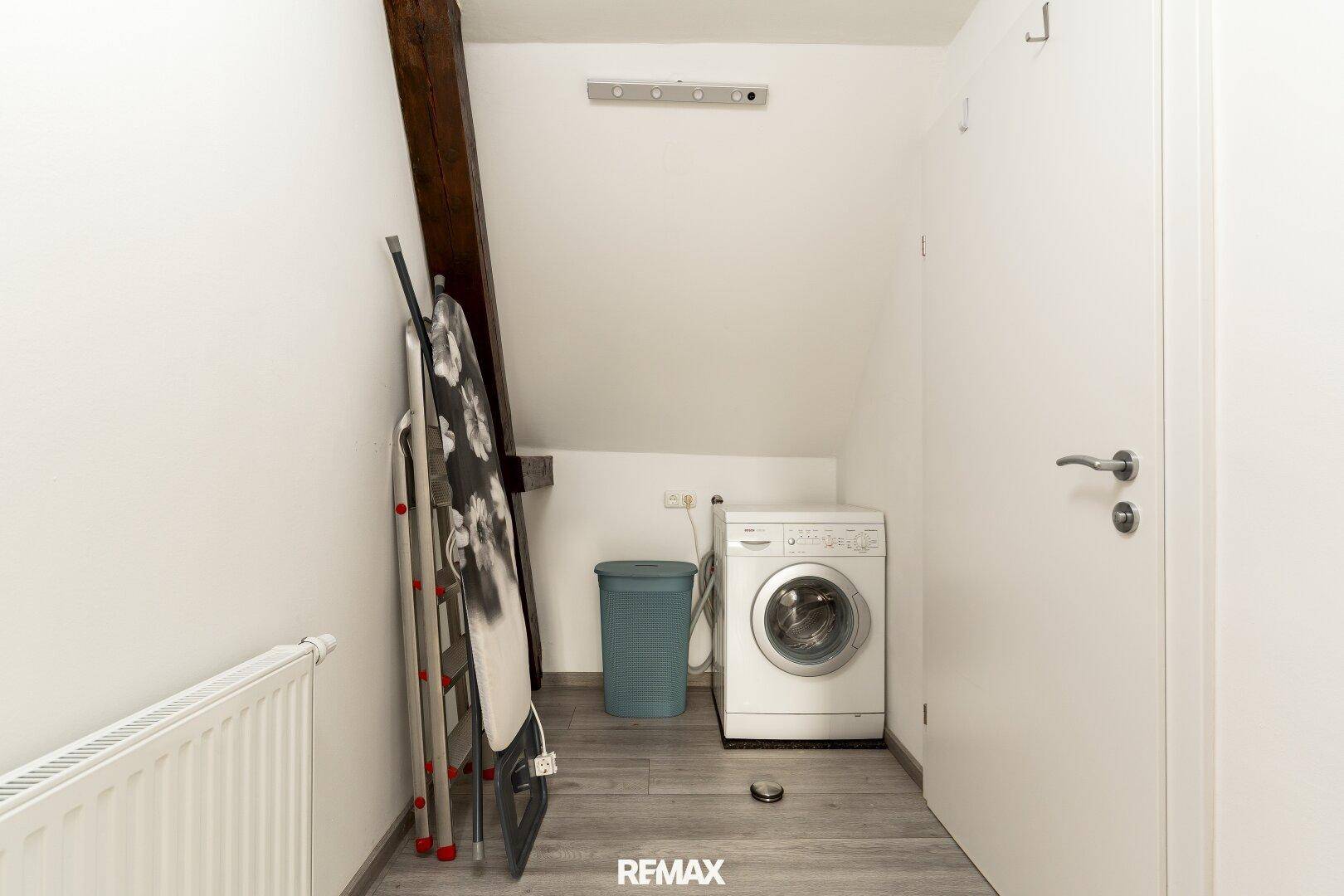 Praktischer Hauswirtschaftsraum im Dachgeschoss mit Waschmaschine und Bügelbrett.
