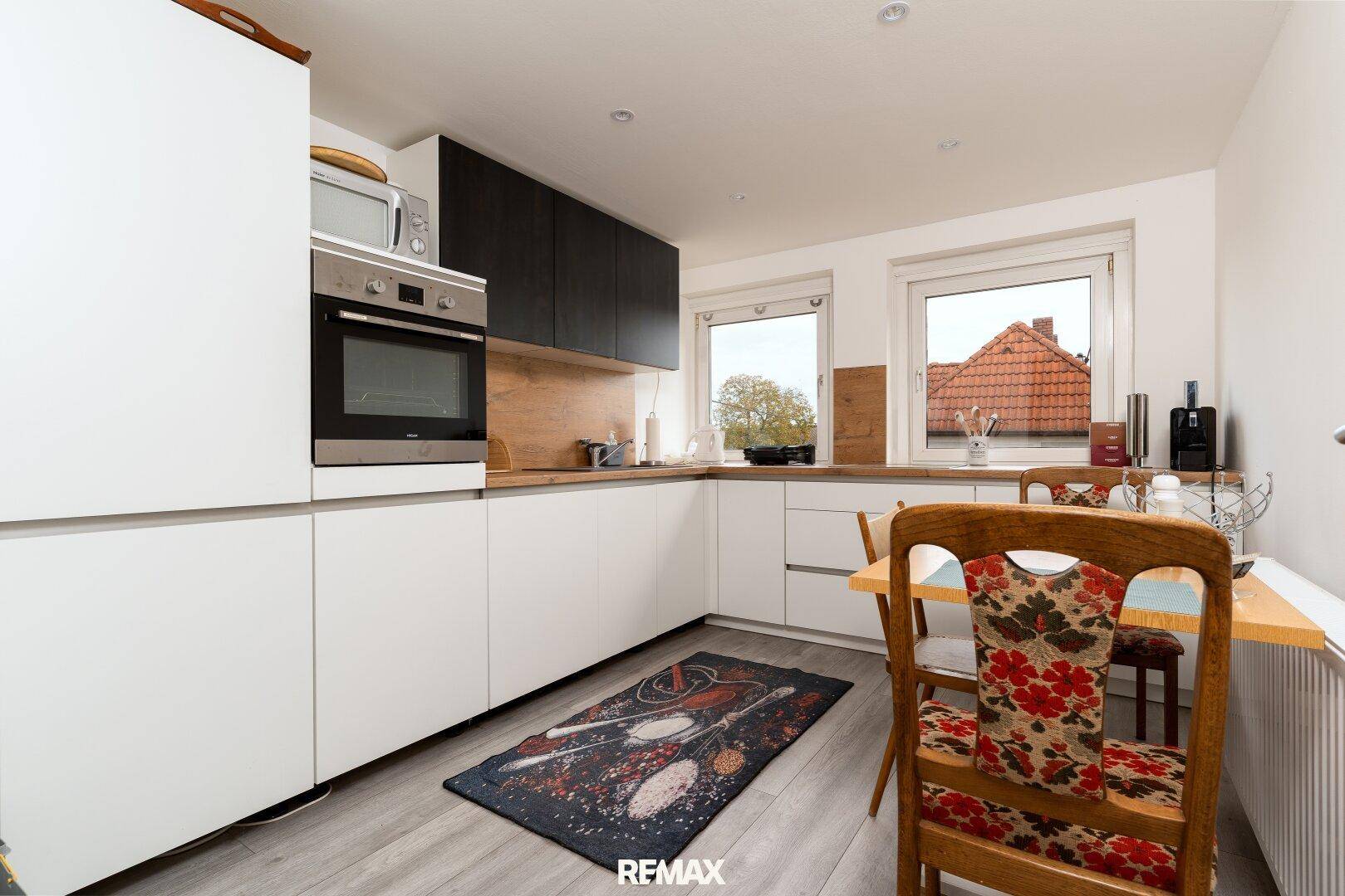 Moderne Küche mit weißen Unterschränken, Holzarbeitsplatte und kleinem Essbereich am Fenster.