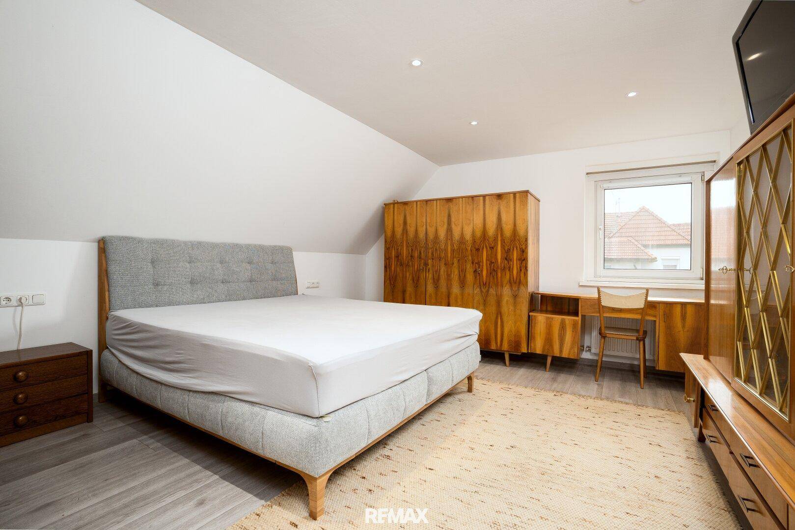Geräumiges Schlafzimmer im Dachgeschoss mit Doppelbett, Holzmöbeln und Fenster.
