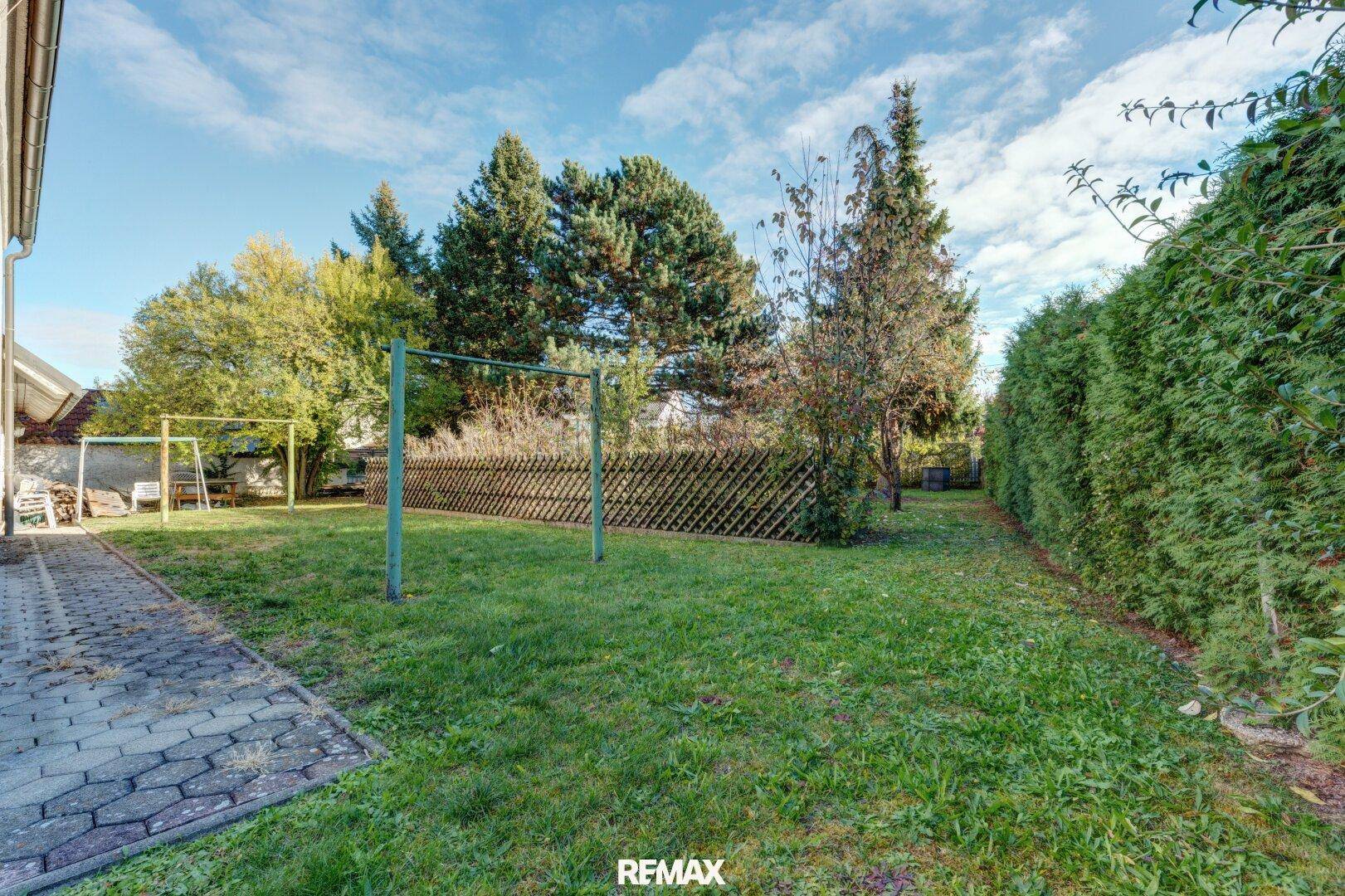 Gepflegter Garten mit Rasenfläche, hoher Hecke und Wäscheleine unter blauem Himmel.