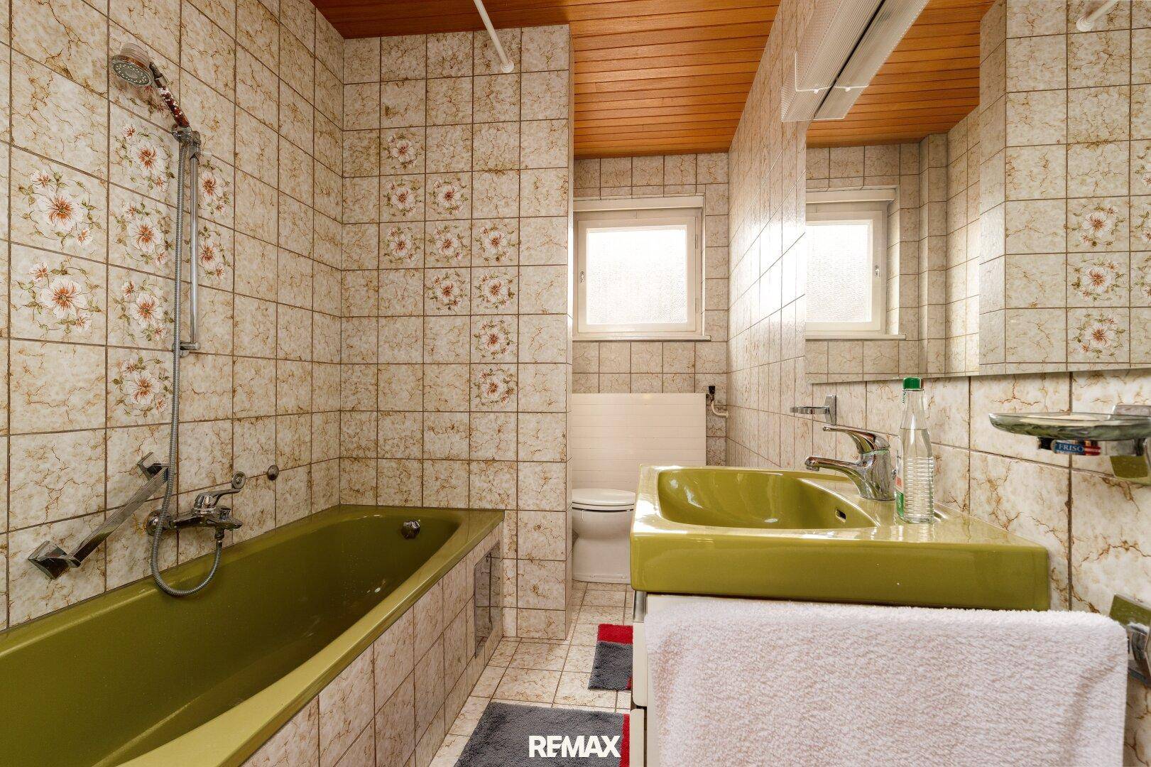 Badezimmer im Stil der 80er Jahre mit gemusterten Fliesen, grüner Badewanne und Waschbecken.