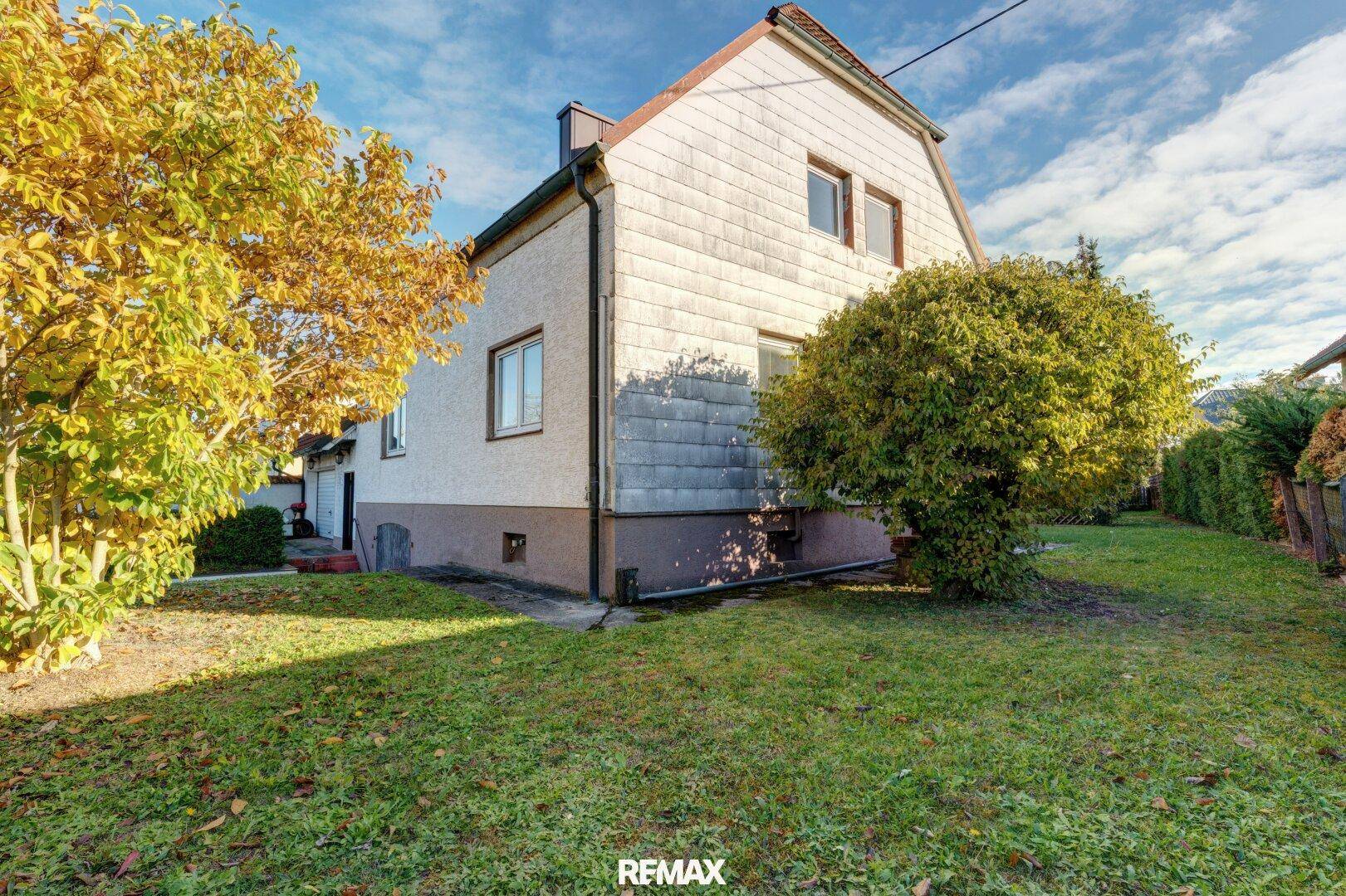 Seitenansicht des Hauses mit gepflegtem Rasen und herbstlicher Bepflanzung.