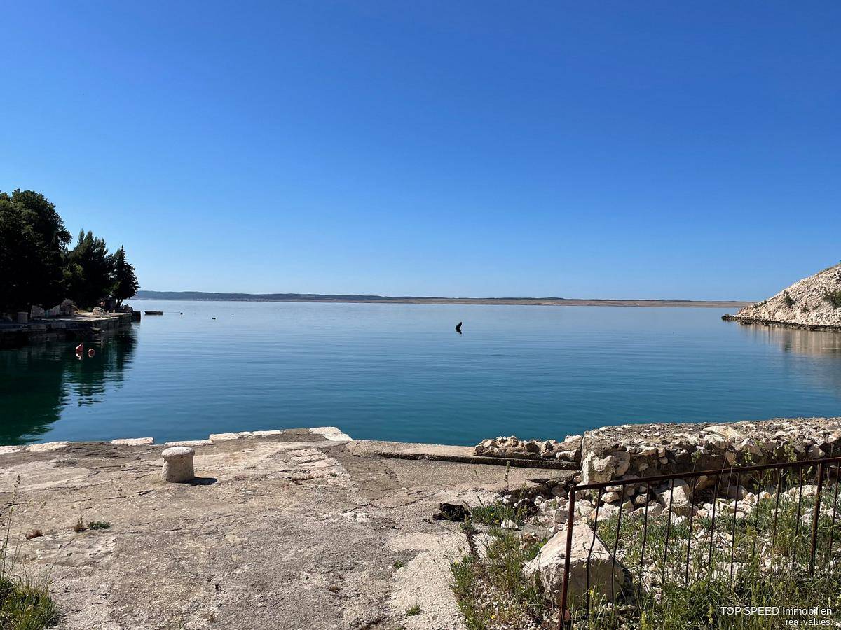 Ruhiges, weites Meer mit klarem Himmel und einer einfachen Betonplattform am Ufer mit etwas Grün.