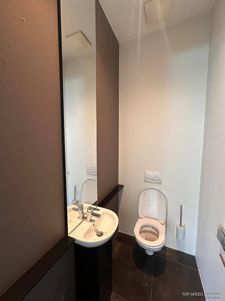 Kompakte Gästetoilette mit modernem Wand-WC, kleinem Waschbecken und großem Wandspiegel.
