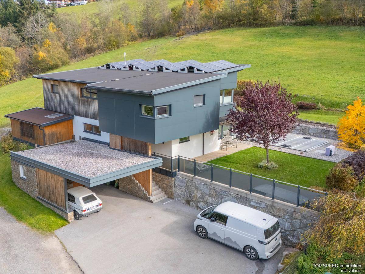 Modernes Haus mit Carport, Photovoltaikanlage und Zufahrt in ländlicher Umgebung.