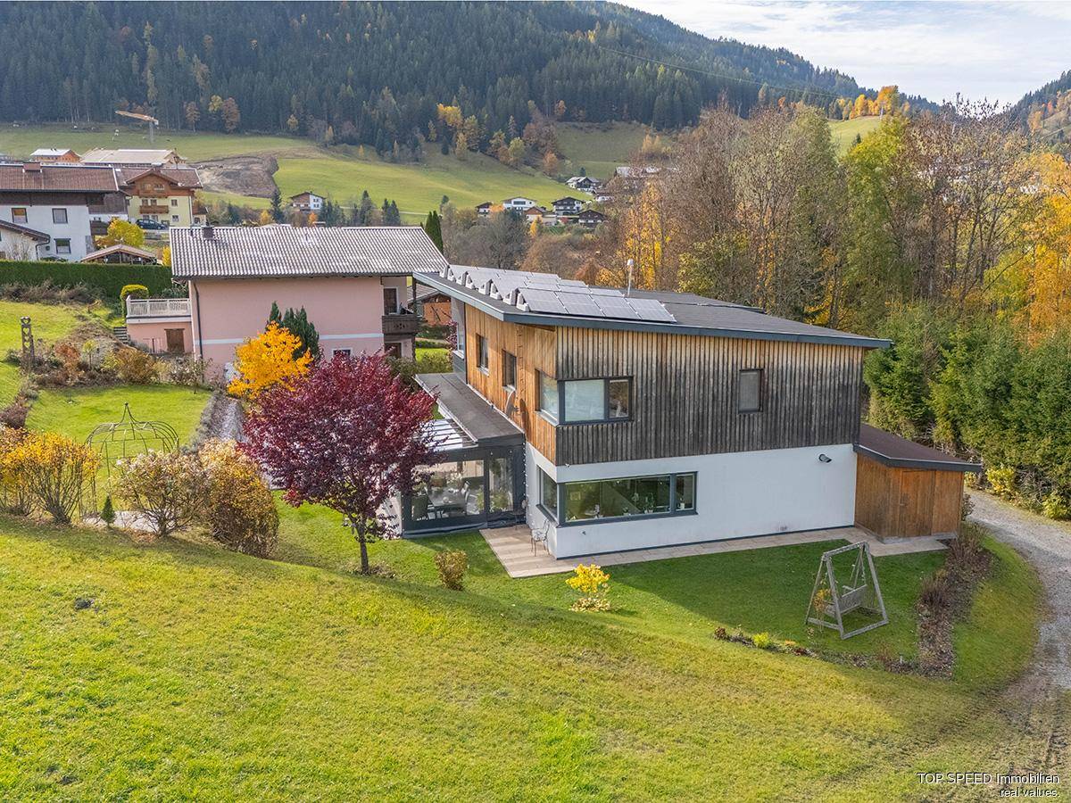 Modernes Haus mit großem Garten, Wintergarten und herbstlicher Landschaft.