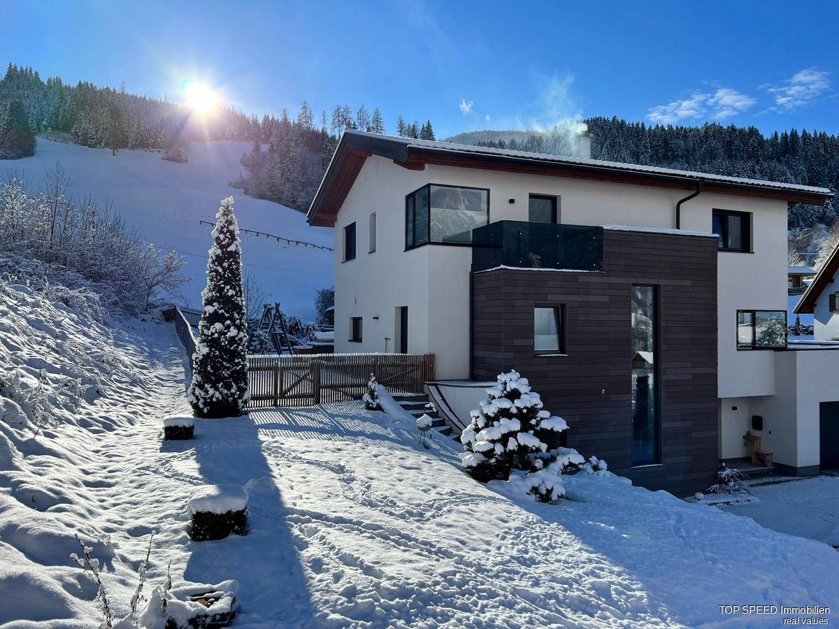 Das moderne Haus in verschneiter Landschaft mit Blick auf die umliegenden Berge und Wälder.