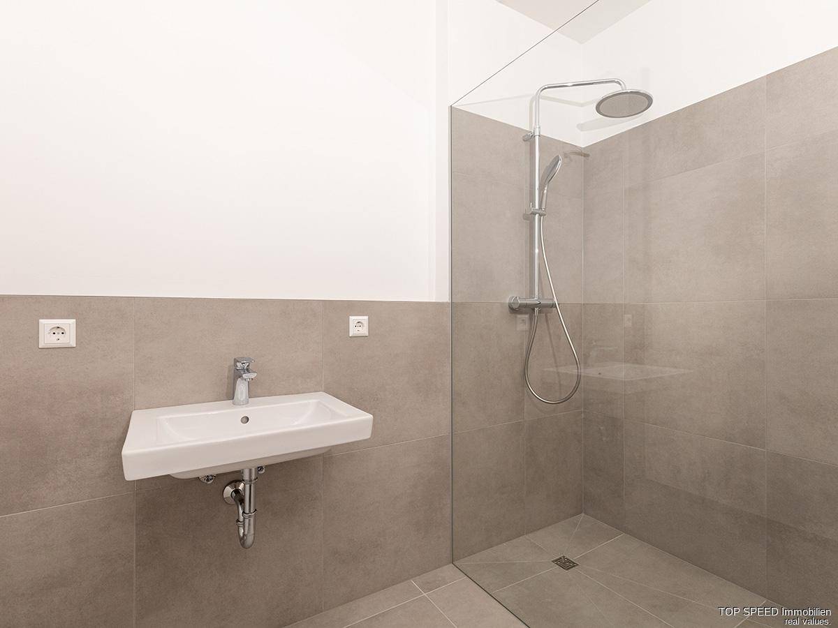 Modernes Badezimmer mit großformatigen Fliesen, bodengleicher Dusche und Einzelwaschbecken.