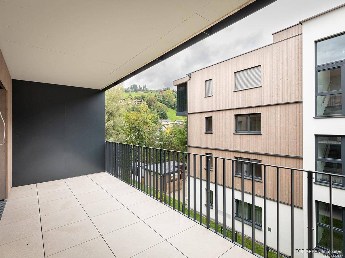 Geräumiger Balkon mit Fliesenboden und Blick auf grüne Hügel und umliegende Gebäude.