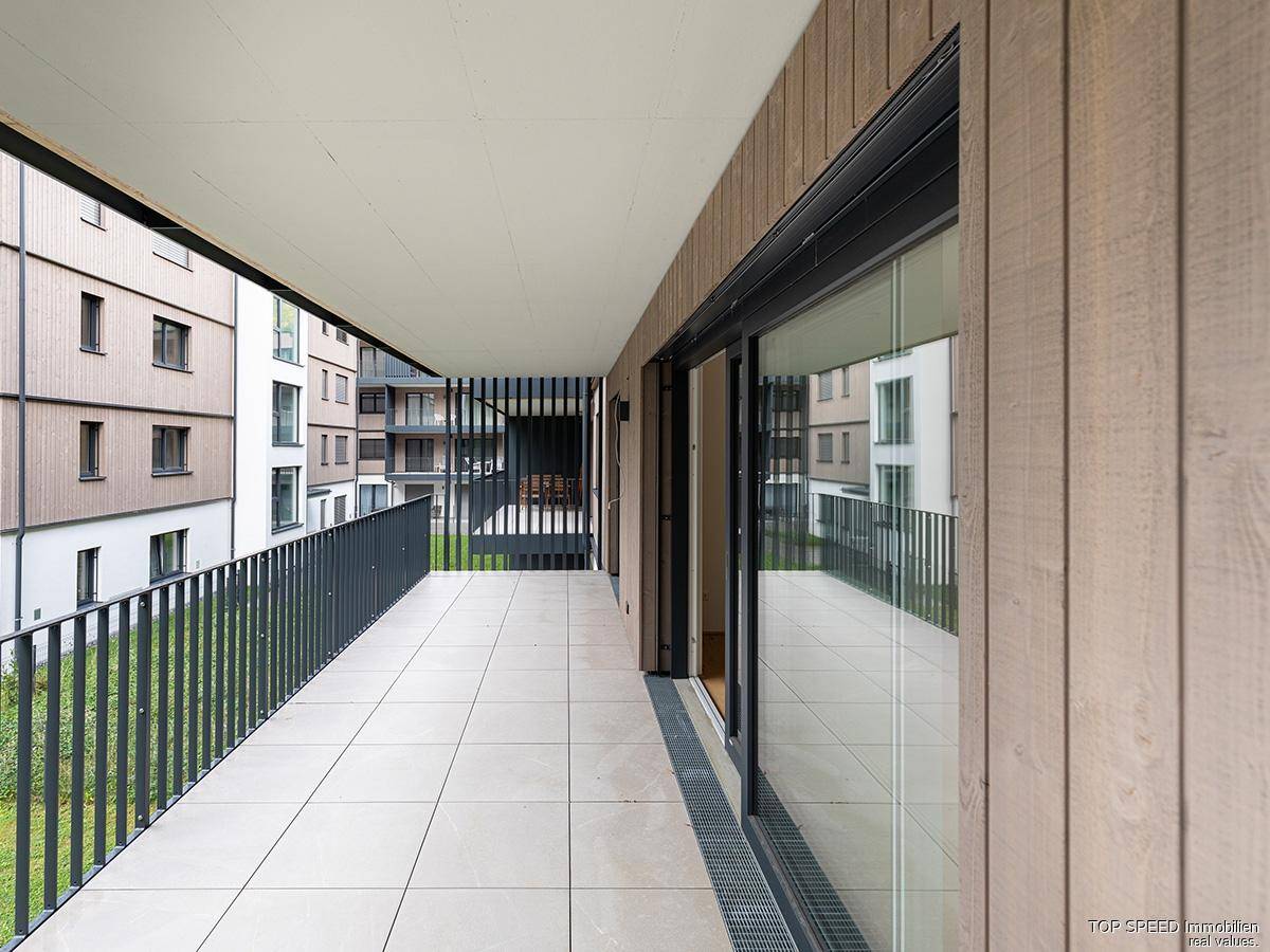 Langer Balkon mit Fliesen und Blick auf die moderne Wohnanlage und die Umgebung.