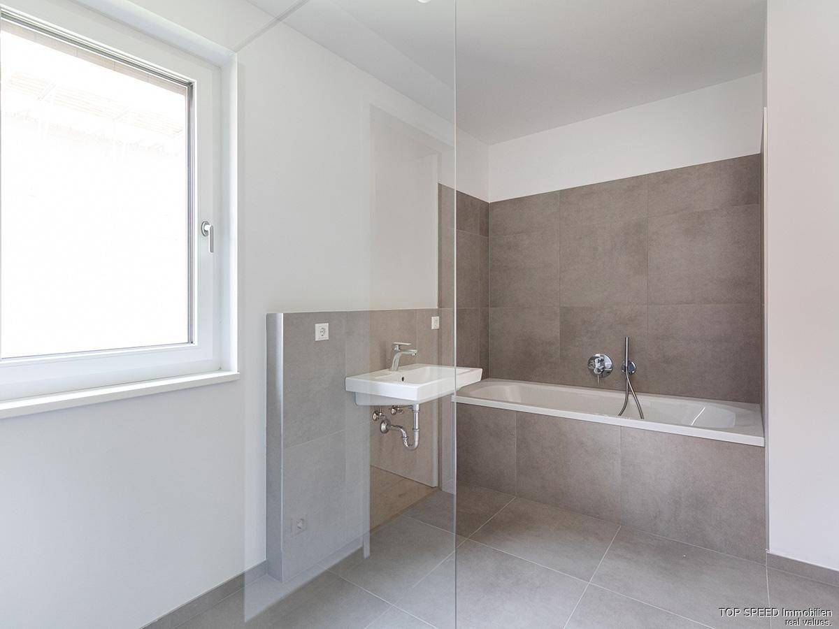 Helles Badezimmer mit Badewanne, Waschbecken und Fenster, modern gefliest.