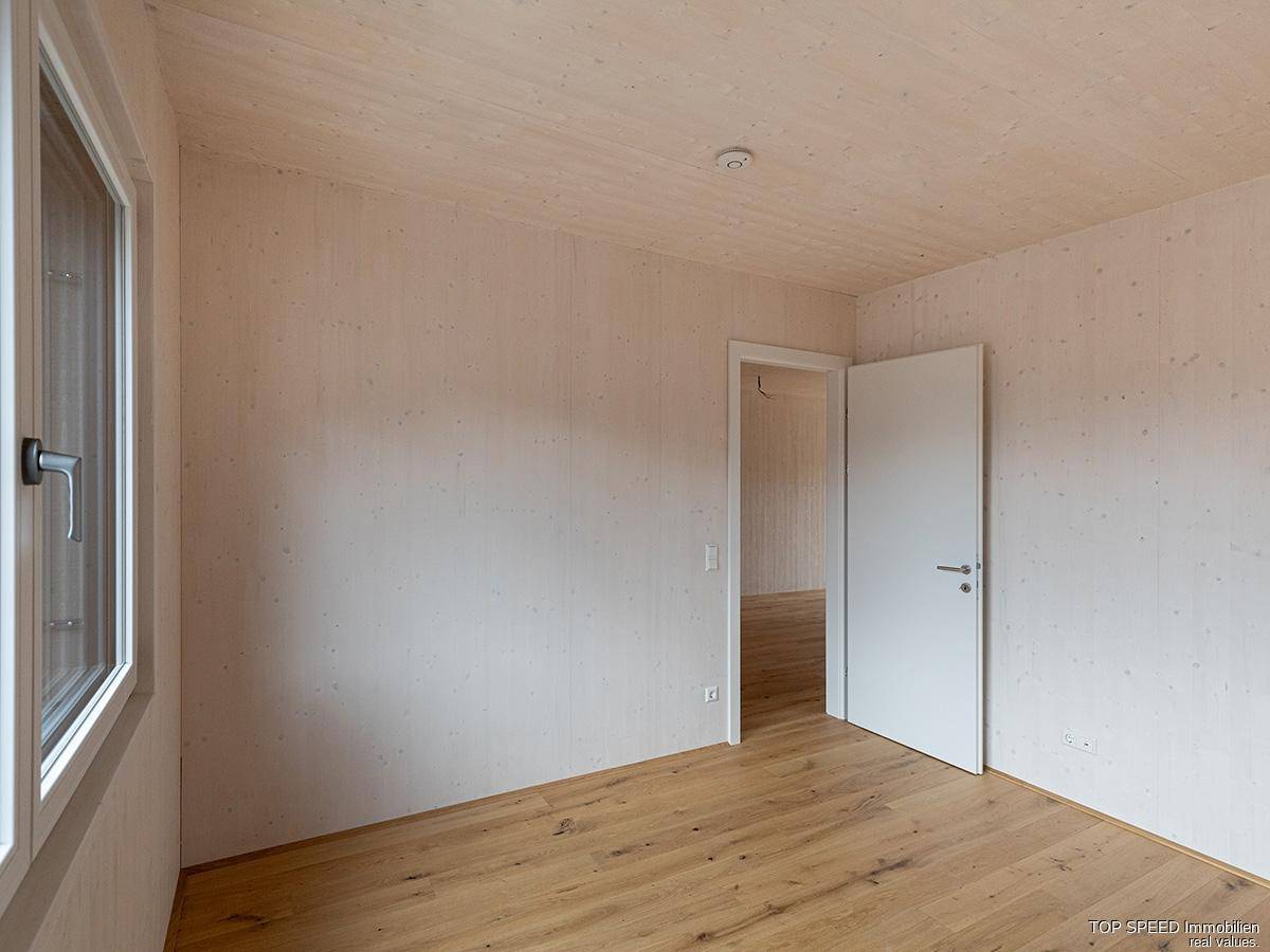 Unmöbliertes Schlafzimmer mit Holzboden und Zugang zu einem weiteren Raum.