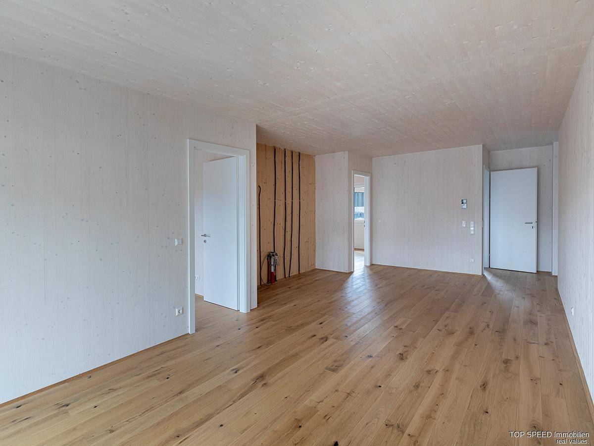 Weitläufiger, unmöblierter Wohnbereich mit hellem Holzboden und mehreren Türzugängen.