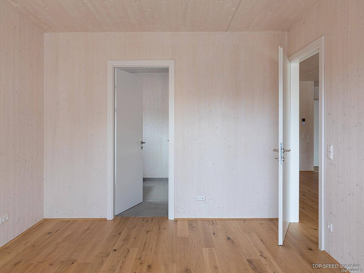 Unmöbliertes Schlafzimmer mit Holzboden und zwei Türöffnungen zu angrenzenden Räumen.