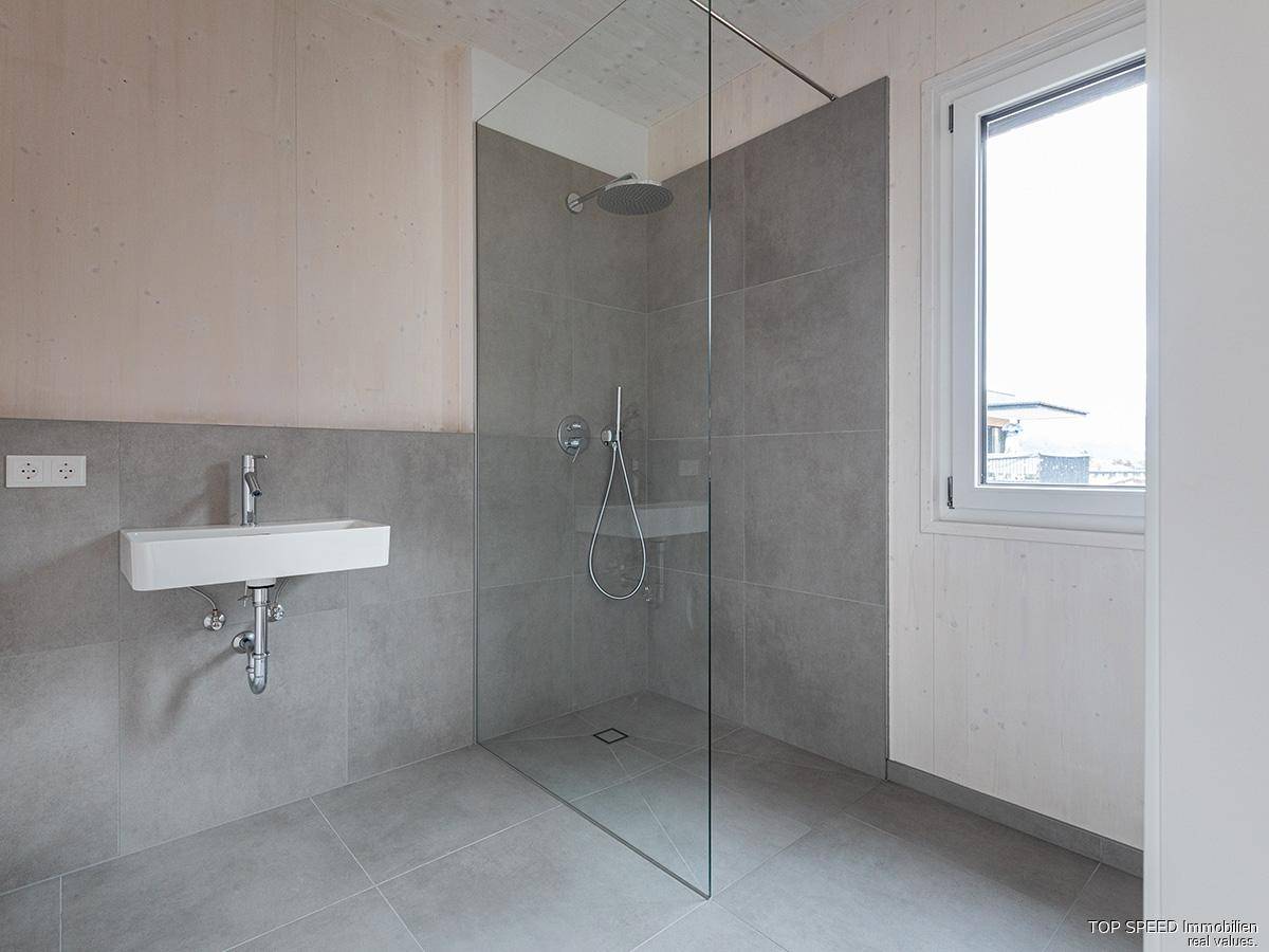 Helles Badezimmer mit bodengleicher Dusche, modernem Waschbecken und Fenster.