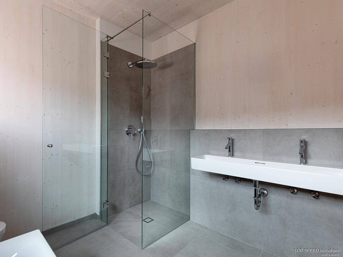 Geräumiges Badezimmer mit bodengleicher Dusche, Doppelwaschbecken und grauen Fliesen.