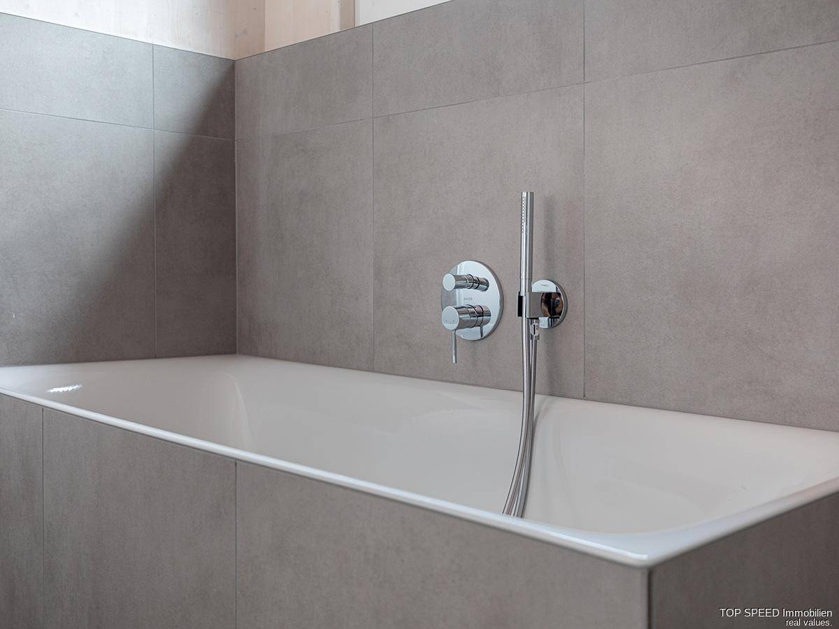Modernes Badezimmer mit eingebauter Badewanne und eleganten grauen Fliesen.
