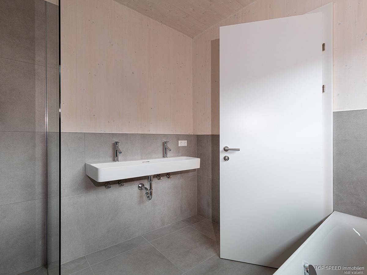 Modernes Badezimmer mit Doppelwaschbecken, grauen Fliesen und einer Badewanne.