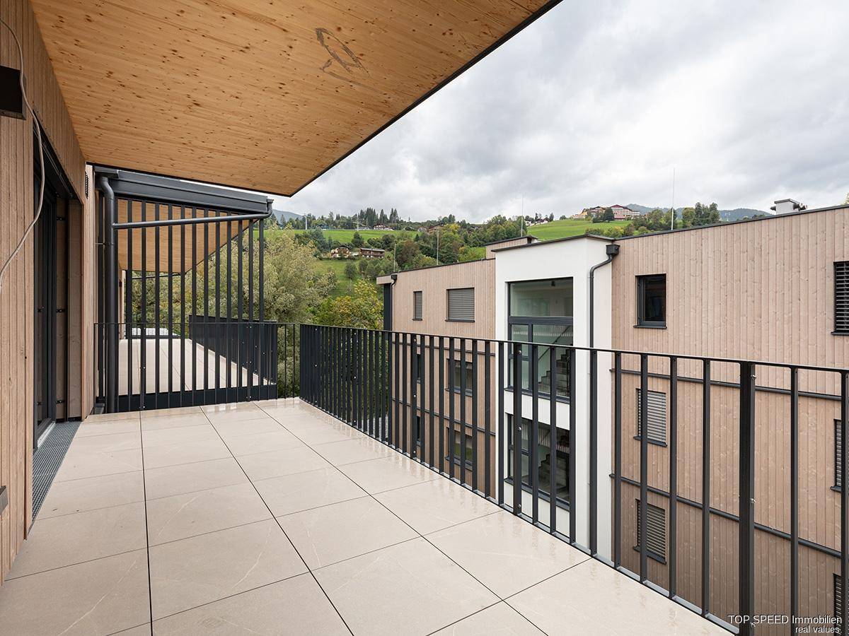 Großer Balkon mit Holzdach, Fliesenboden und weitem Blick auf die grüne Landschaft.