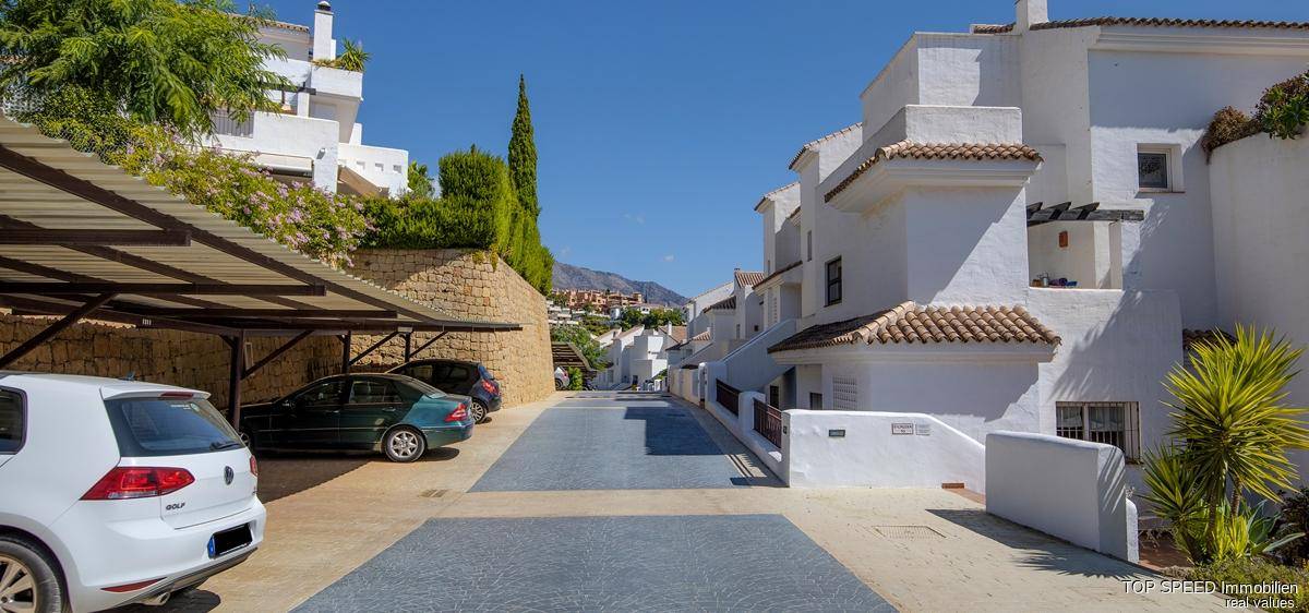 Weiße Gebäude im mediterranen Stil mit überdachten Parkplätzen und gepflegter Umgebung.
