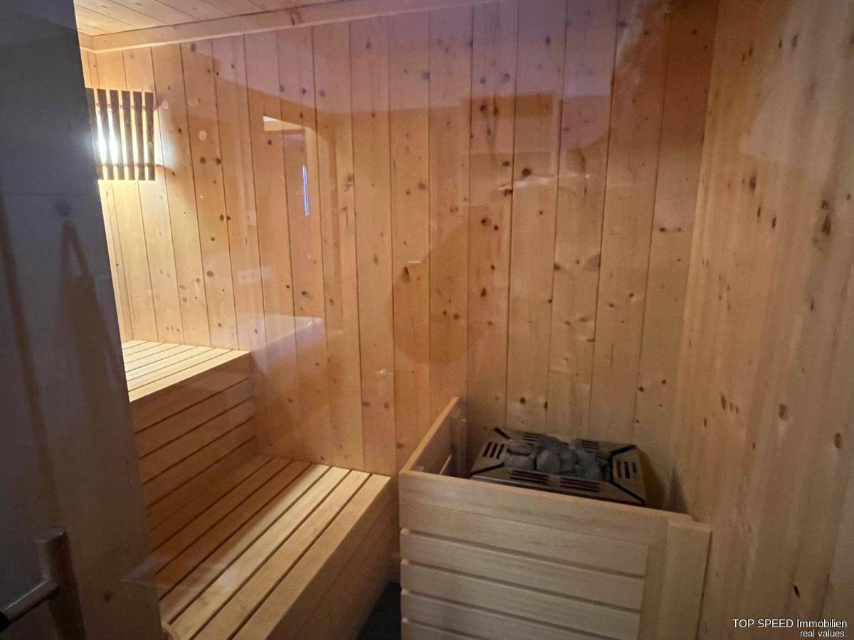 Innenansicht der holzverkleideten Sauna mit Sitzbänken und Heizofen für Wellnessmomente.