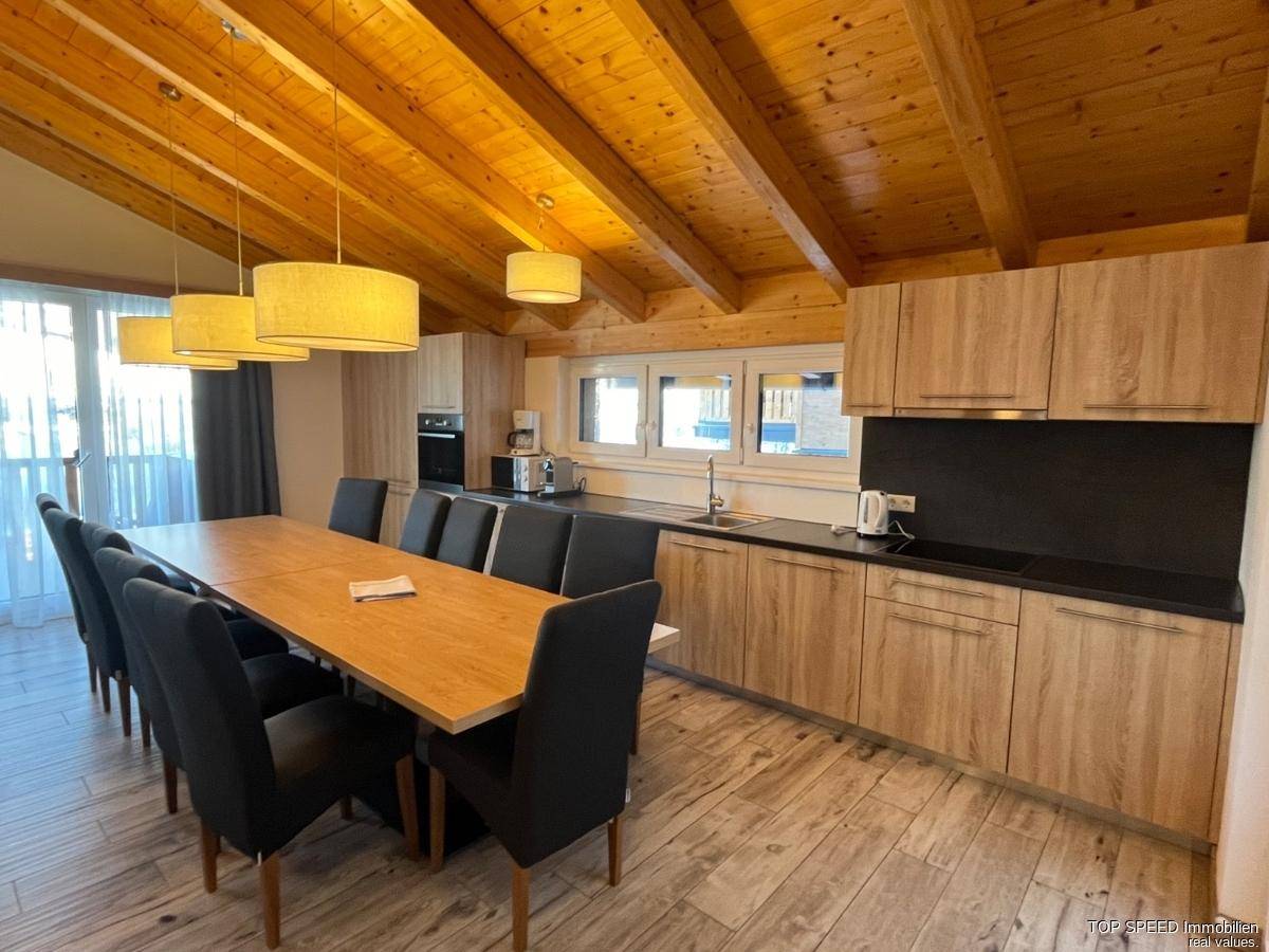 Geräumige Wohnküche mit Holzbalkendecke, großem Esstisch und modernen Küchengeräten.