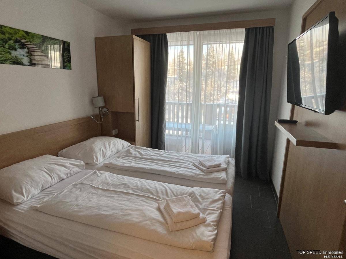 Helles Schlafzimmer mit zwei Einzelbetten, Kleiderschrank und Zugang zu einem Balkon.