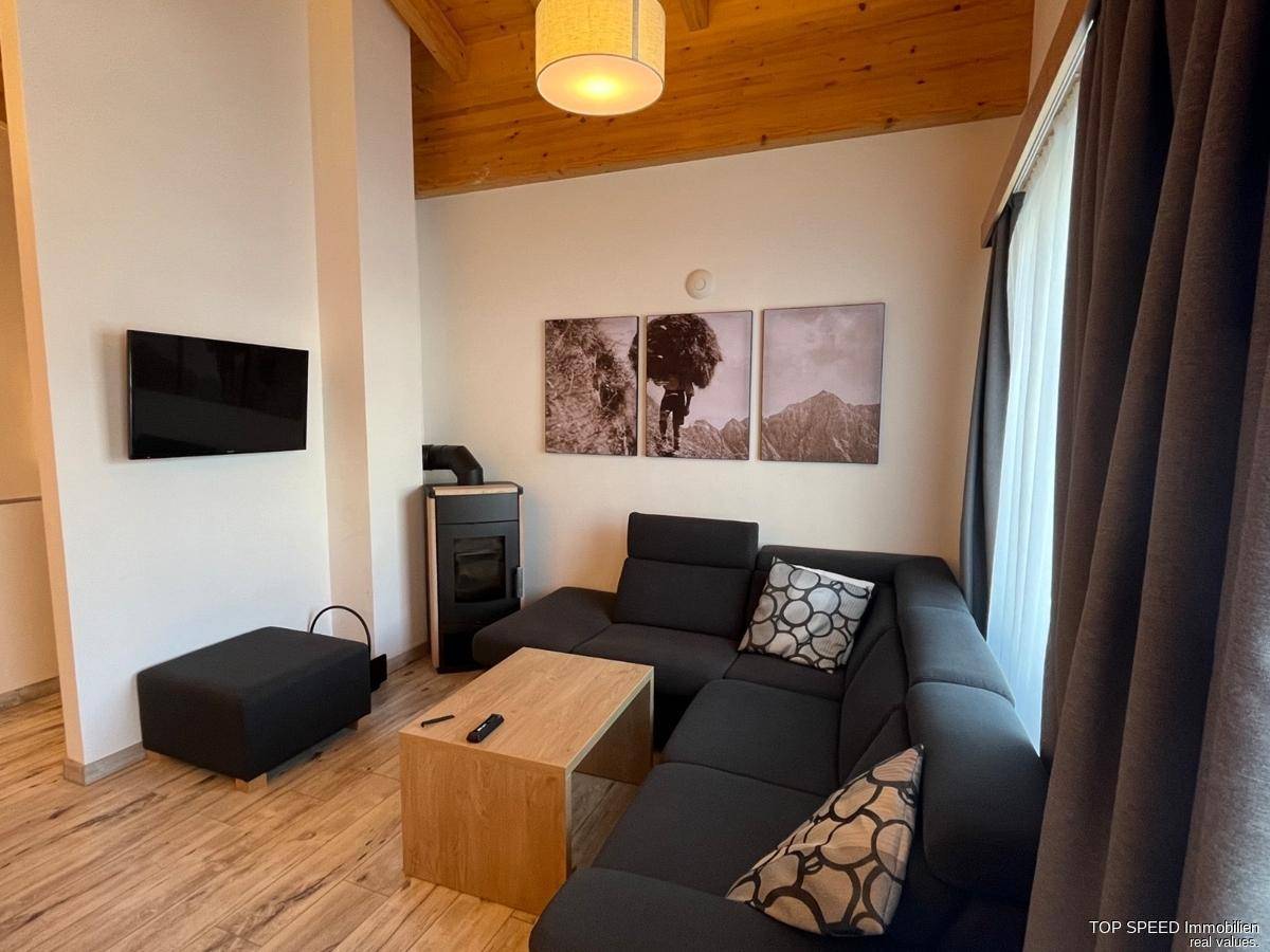 Gemütliches Wohnzimmer mit Holzbalkendecke, modernem Kaminofen und bequemer Eckcouch.