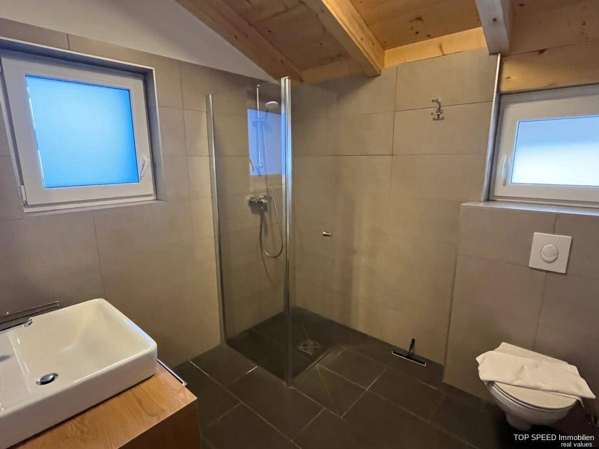 Modernes Badezimmer mit ebenerdiger Dusche, Einzelwaschbecken und zwei Fenstern.