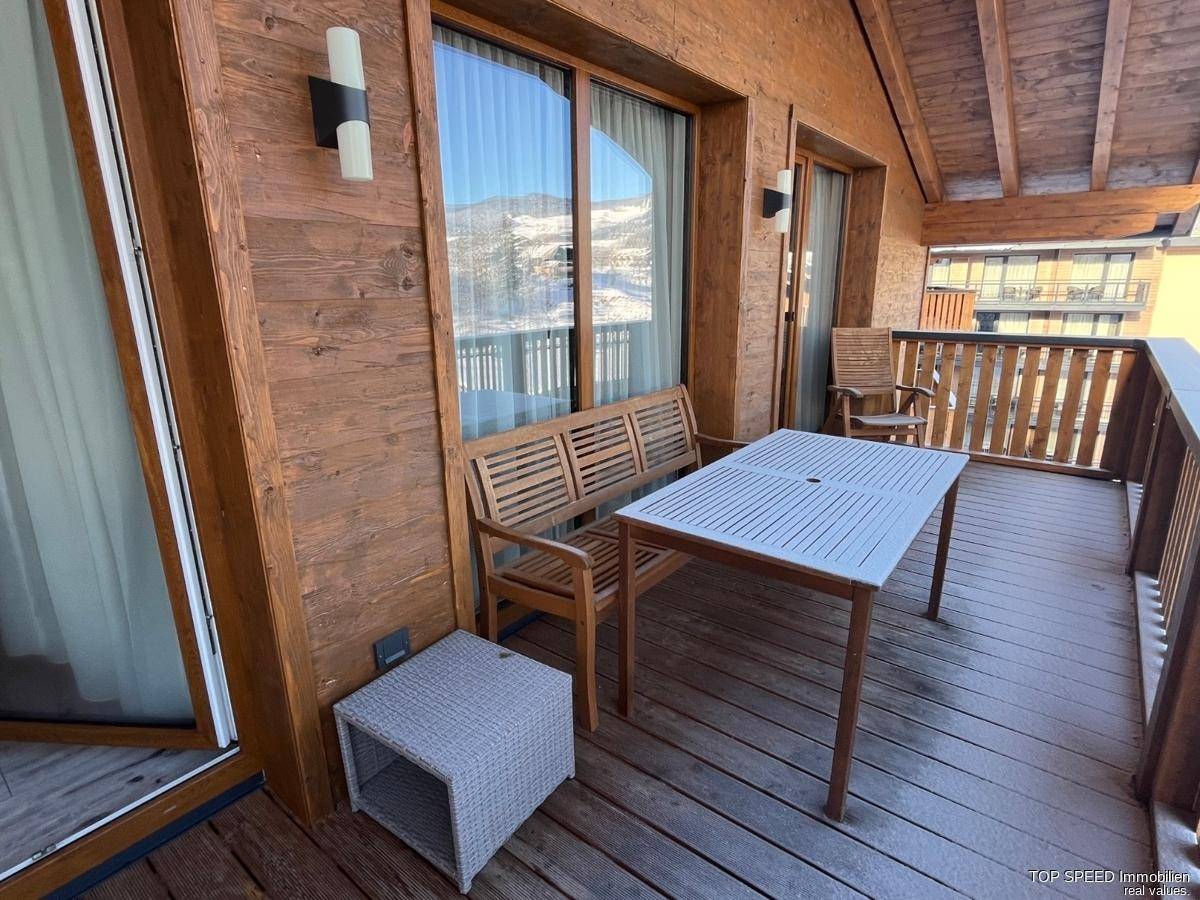 Geräumiger Holzbalkon mit Sitzgelegenheiten und Blick auf die umliegende Berglandschaft.
