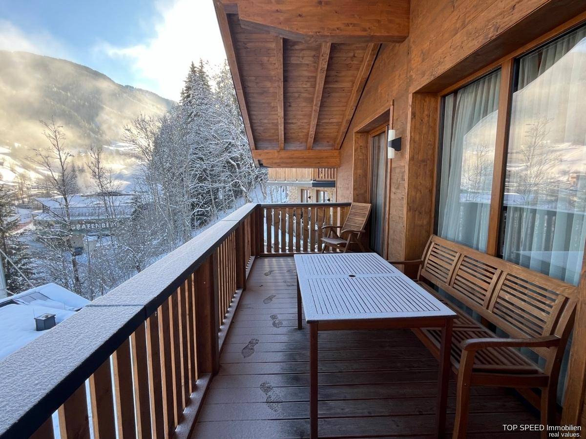 Breiter Holzbalkon mit Esstisch und Bank, bedeckt mit leichtem Schnee, bietet Bergblick.