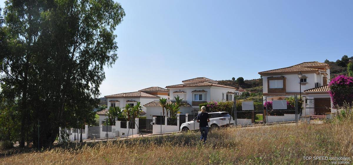 Wohngebiet mit mehreren Häusern im mediterranen Stil, umgeben von trockener Vegetation.