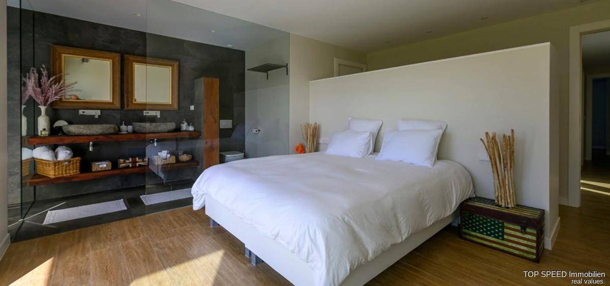 Modernes Schlafzimmer mit Holzboden und offenem Badezimmerbereich mit Doppelwaschbecken.