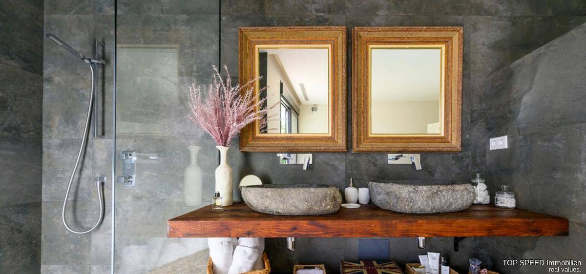 Elegantes Badezimmer mit zwei Steinwaschbecken, Holzablage und großer begehbarer Dusche.