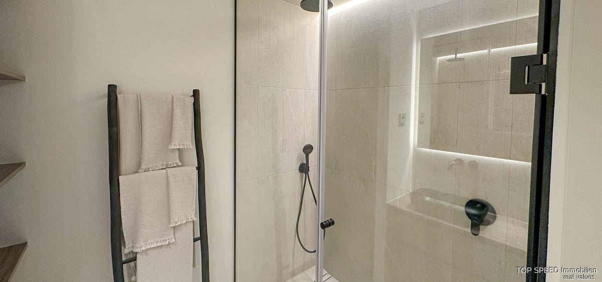 Moderne begehbare Dusche mit Glasabtrennung und Regenduschkopf in hellem Badezimmer.