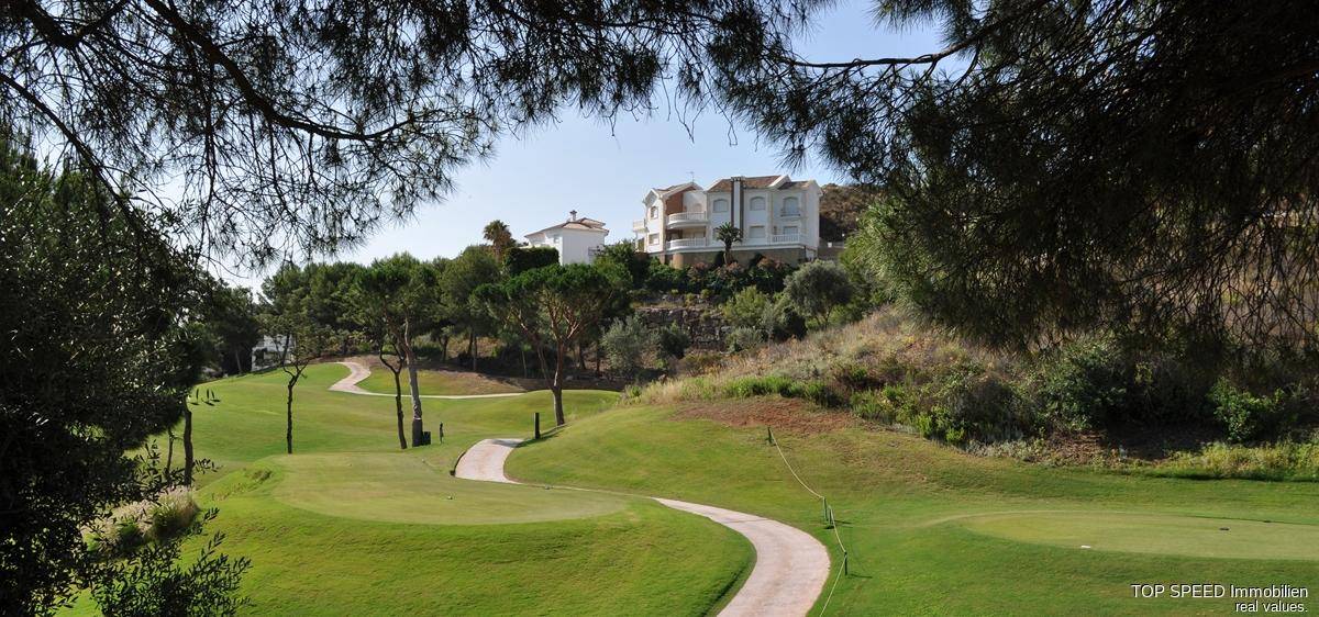 Malerischer Golfplatz mit gewundenen Wegen und Wohnhäusern in der Ferne, umgeben von Bäumen.