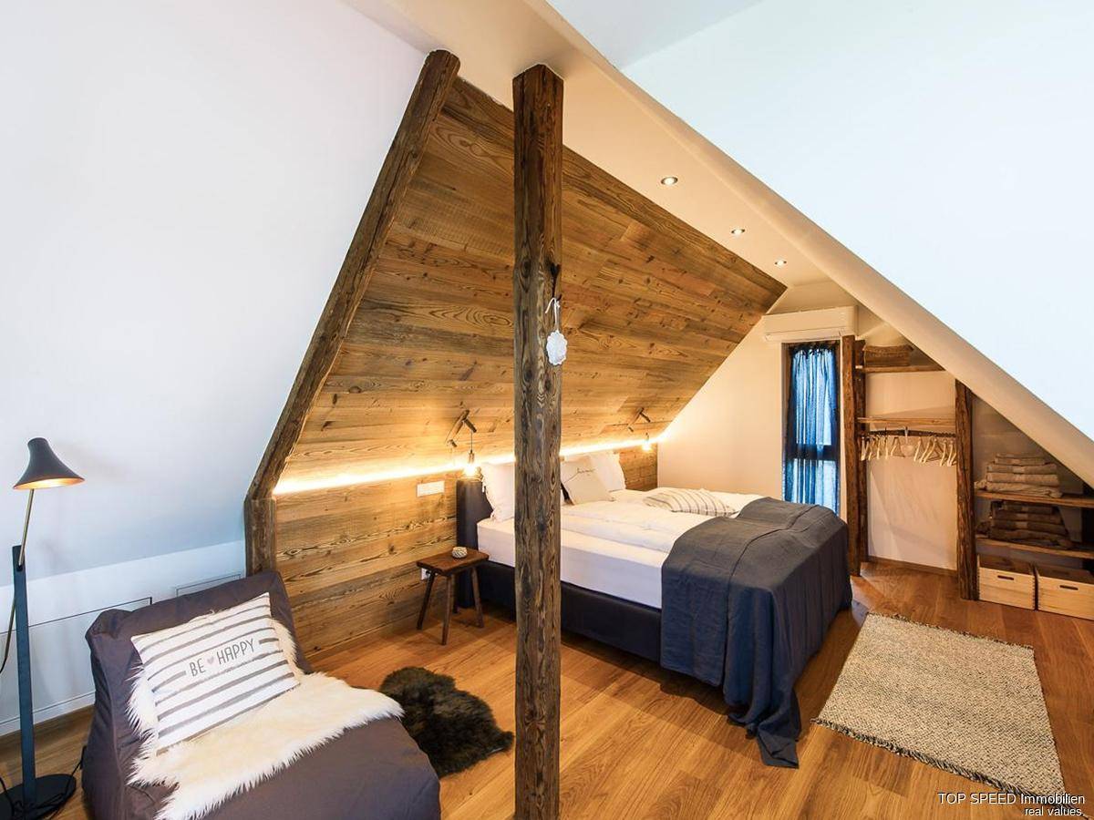 Gemütliches Schlafzimmer im Dachgeschoss mit Holzwand, indirekter Beleuchtung und offenem Kleiderschrank.