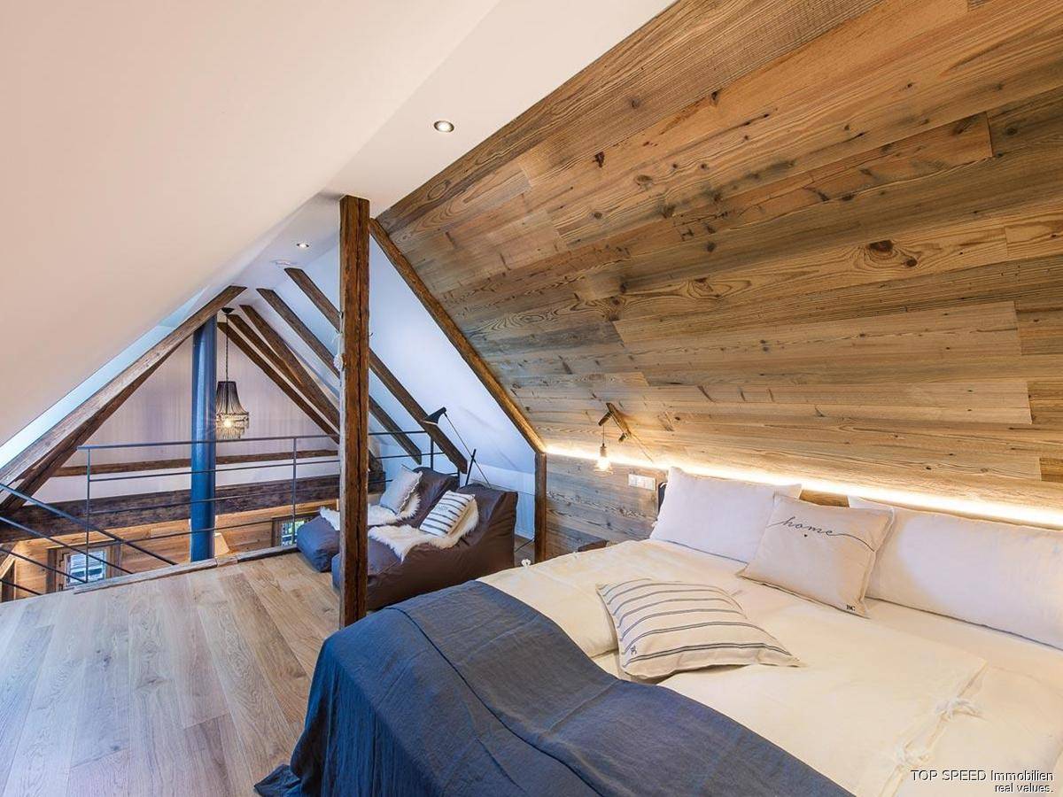 Schlafzimmer mit Holzwand und Blick auf den darunterliegenden Wohnbereich und die Galerie.