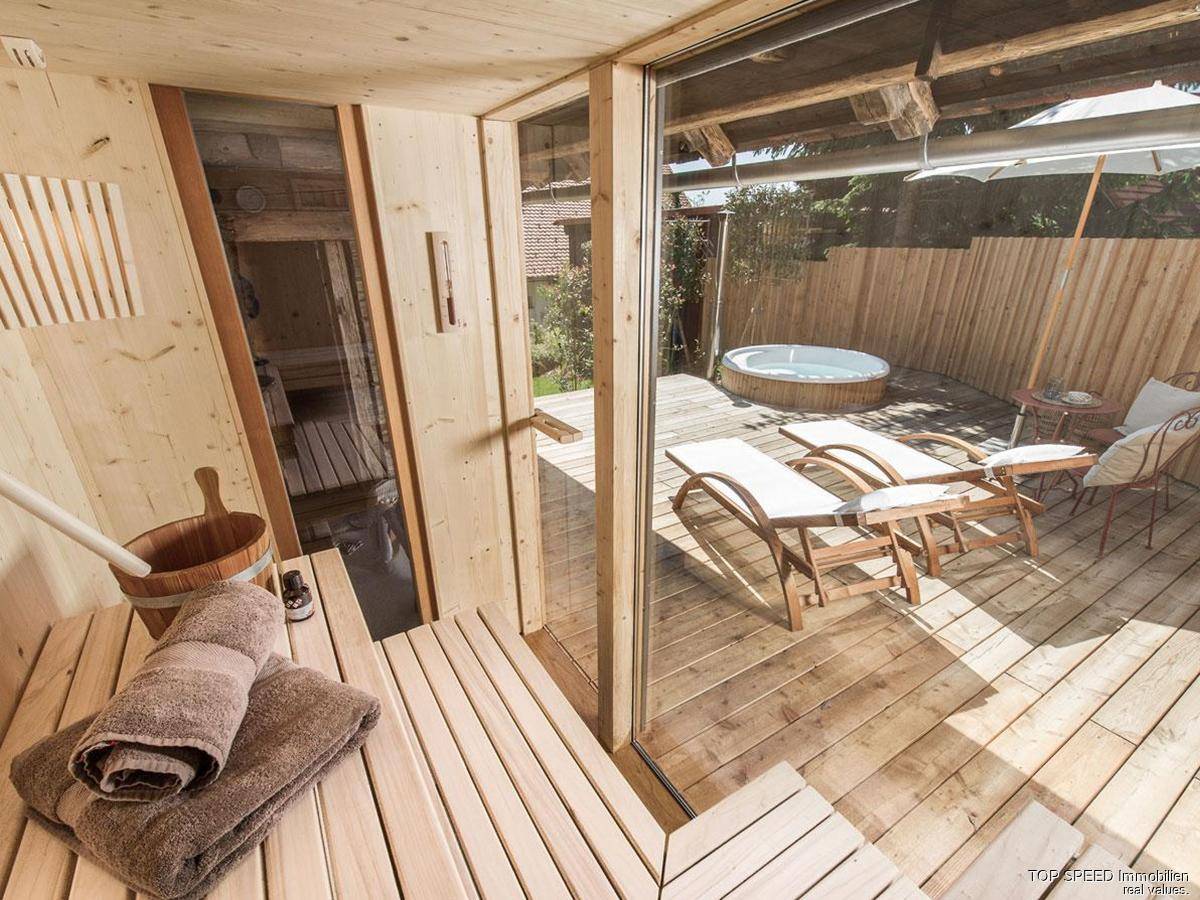 Holzterrasse mit Whirlpool, Liegestühlen und Zugang zur Sauna im Freien.