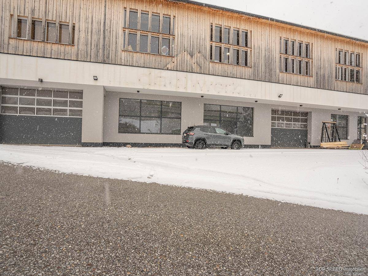 Moderne Holzfassade des Gebäudes mit großen Fenstern und Rolltoren, umgeben von Schnee.