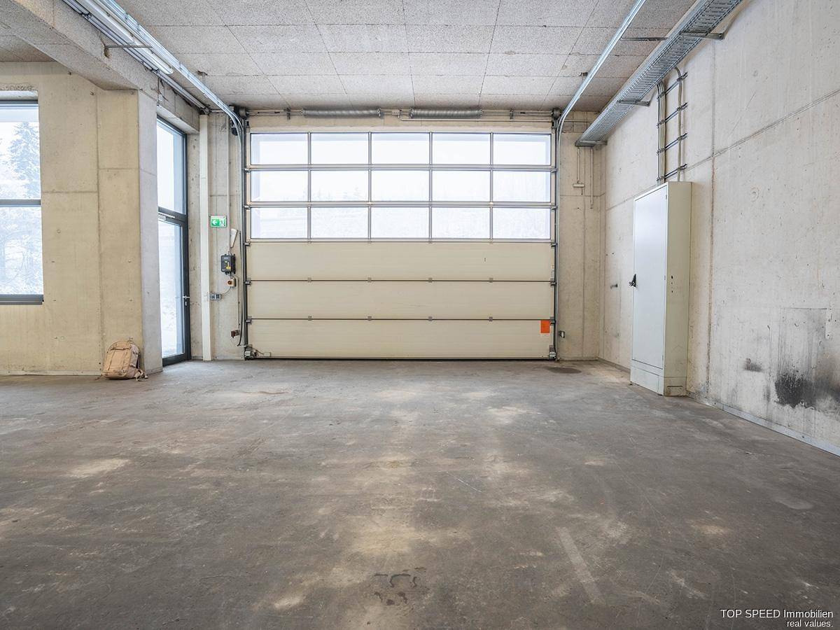 Geräumiger Gewerberaum mit Betonboden, Rolltor und hohen Decken, geeignet für Anlieferung und Lagerung.
