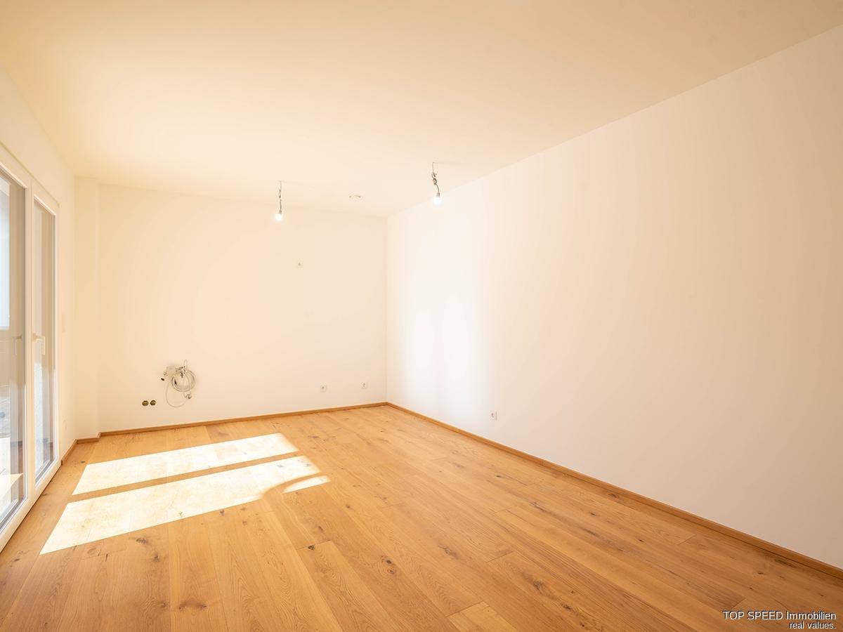 Geräumiges, unmöbliertes Zimmer mit Holzboden und großen Fenstern für viel Tageslicht.