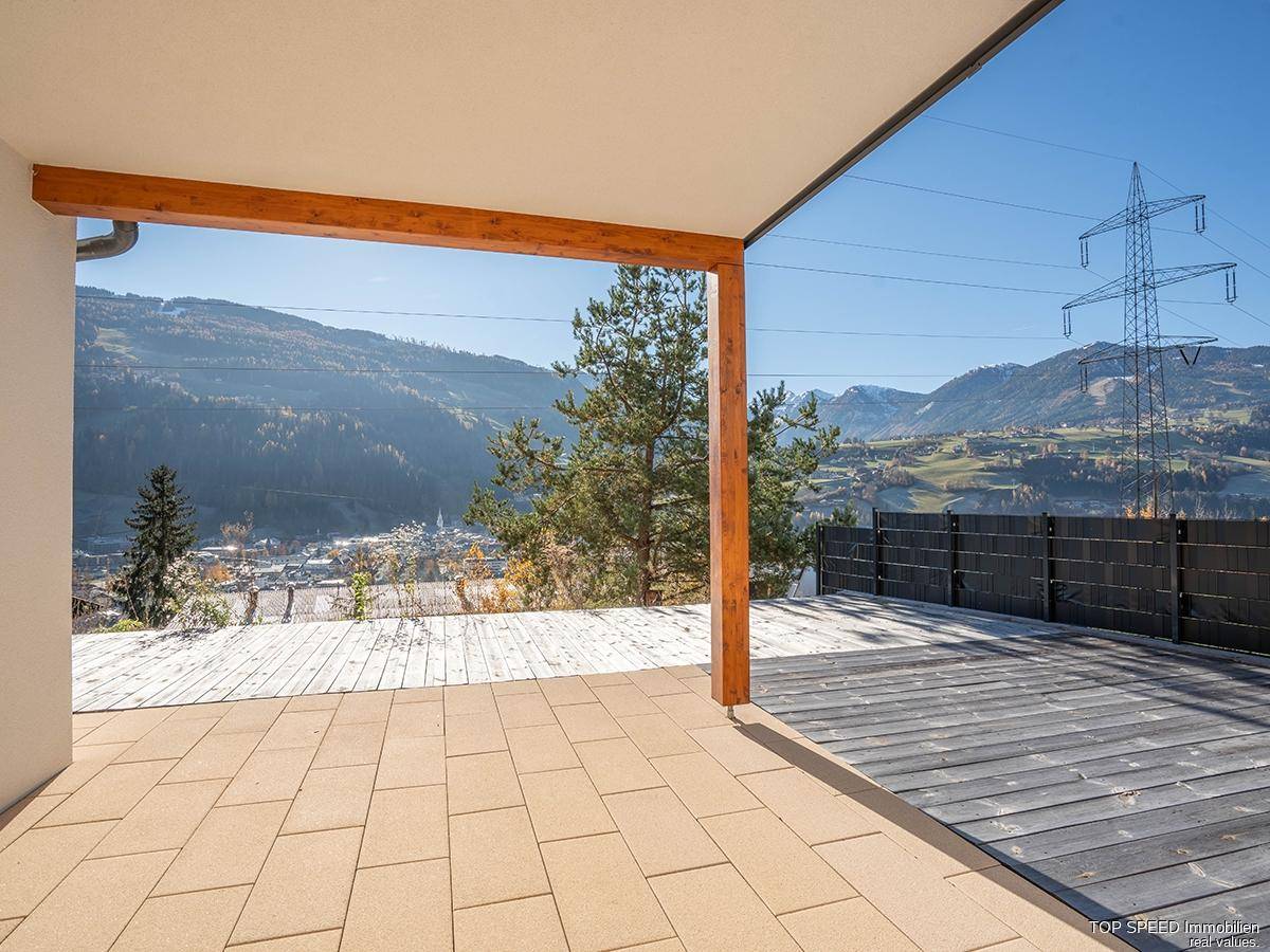 Geräumige Terrasse mit Holzdielen und Fliesen, die einen weiten Blick auf die Berge und das Tal bietet.