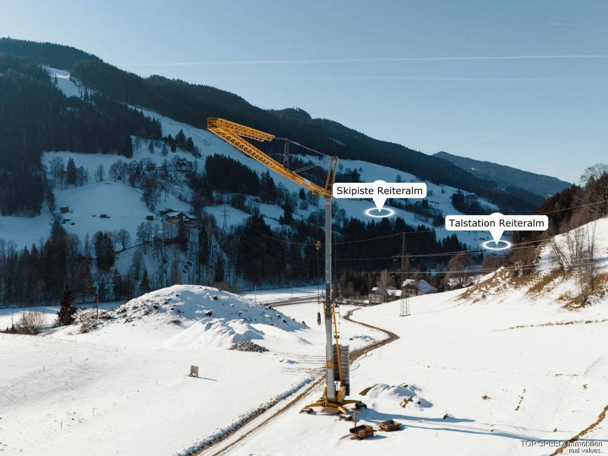 Luftaufnahme einer Baustelle in verschneiter Landschaft mit Kran und Hinweisen auf die Skipiste Reiteralm.