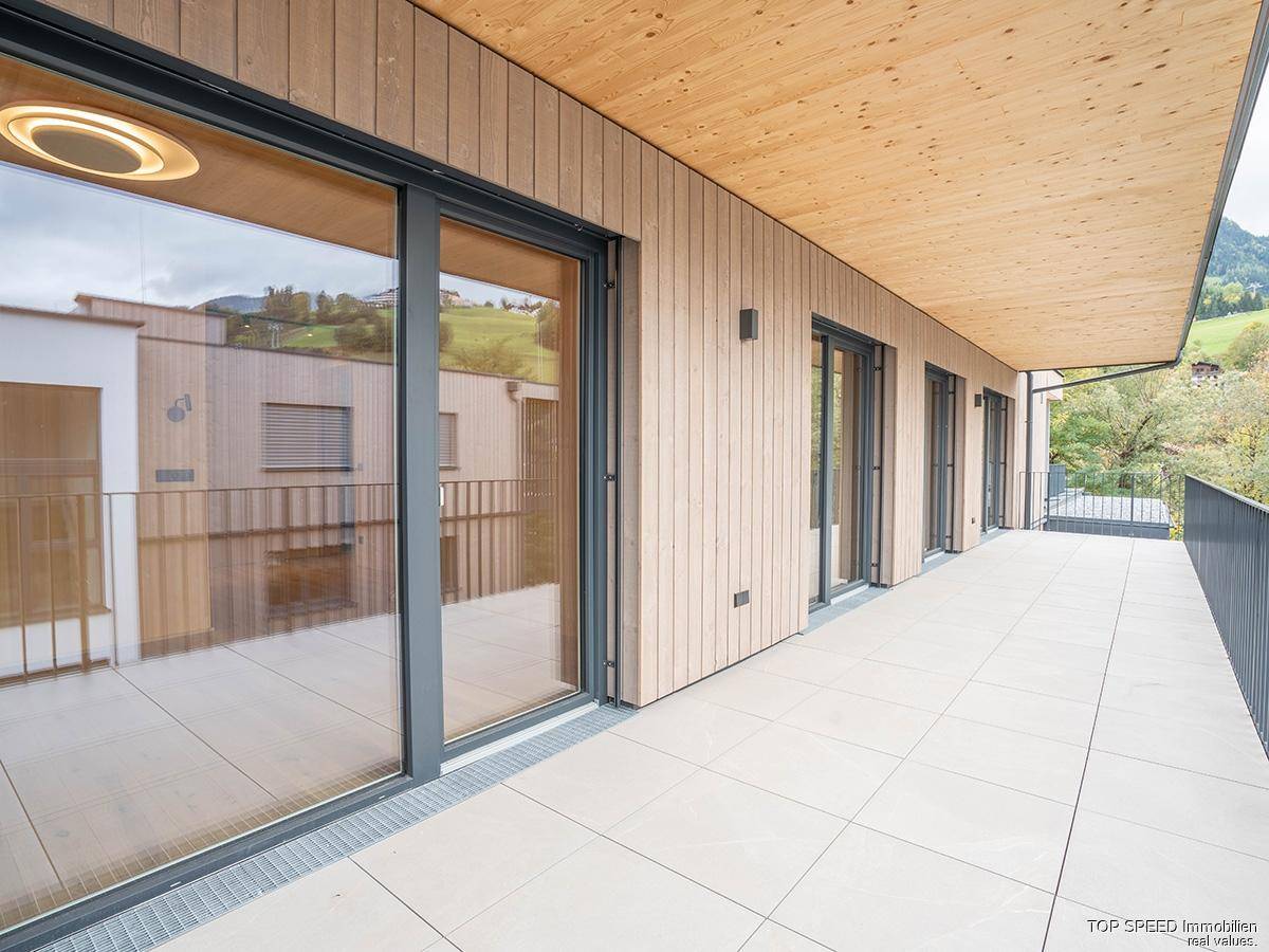 Moderne Gebäudefassade mit großen Glasfronten und einer weitläufigen, gefliesten Terrasse.