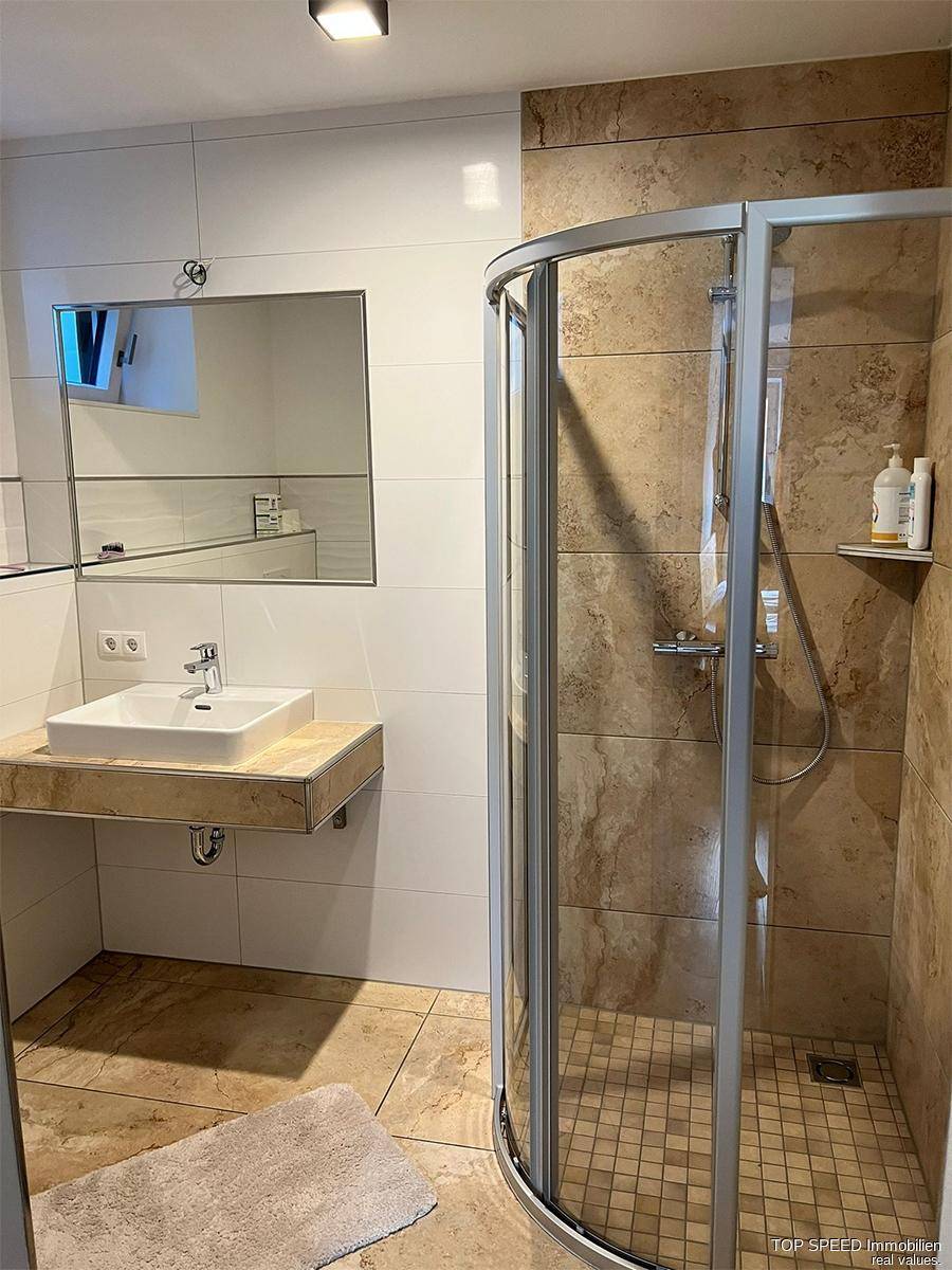 Badezimmer mit moderner Duschkabine, Einzelwaschbecken und hellen Fliesen.