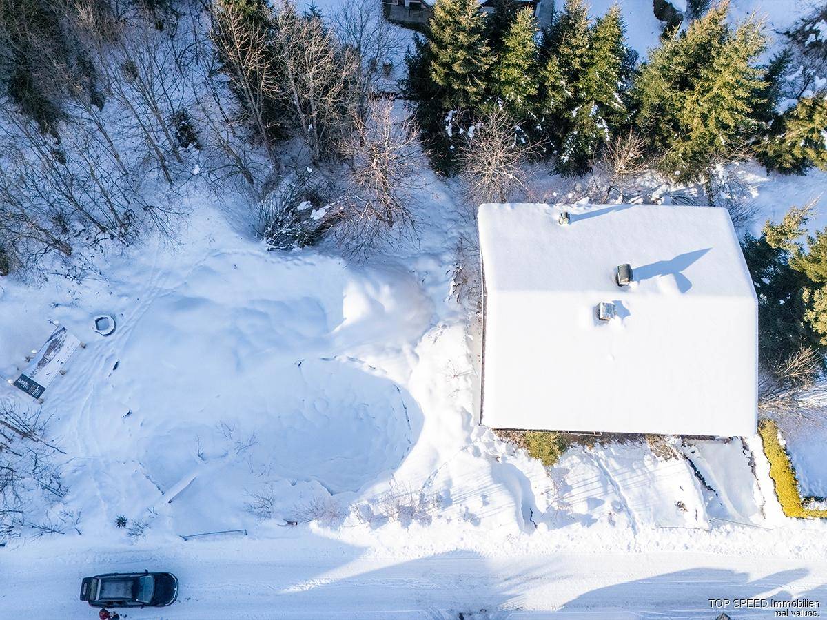Luftaufnahme eines Hauses mit schneebedecktem Dach und umliegender Winterlandschaft.