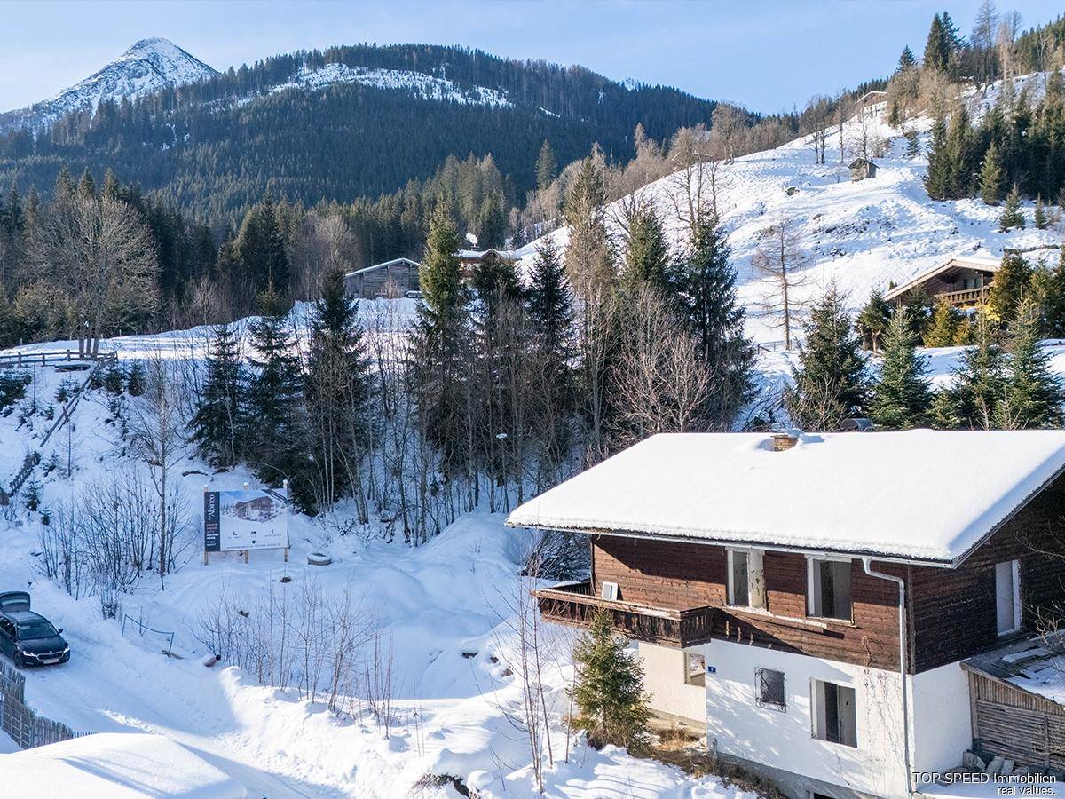 Traditionelles Haus in einer verschneiten Berglandschaft mit weiteren Gebäuden im Hintergrund.