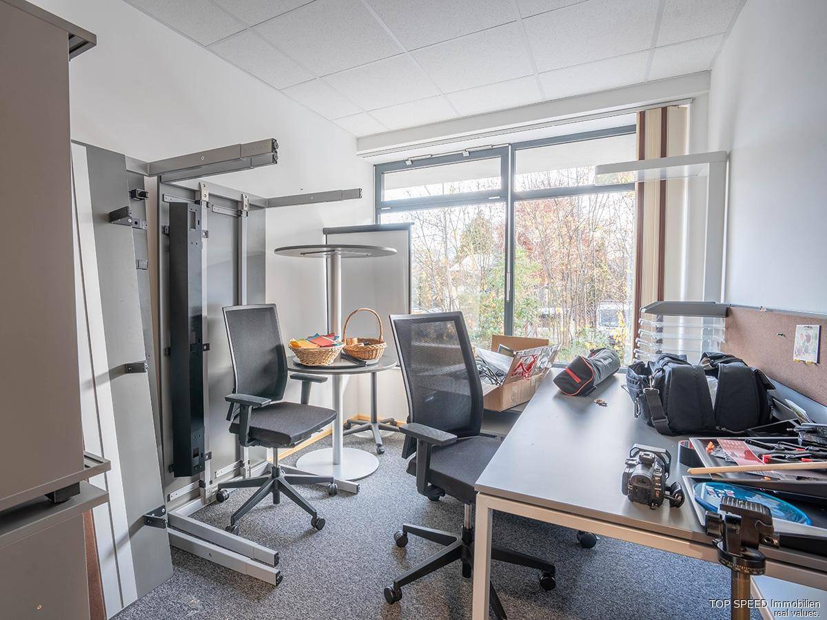 Flexibler Bürobereich mit Stehtisch, Bürostühlen und Blick auf die Umgebung durch die Fenster.